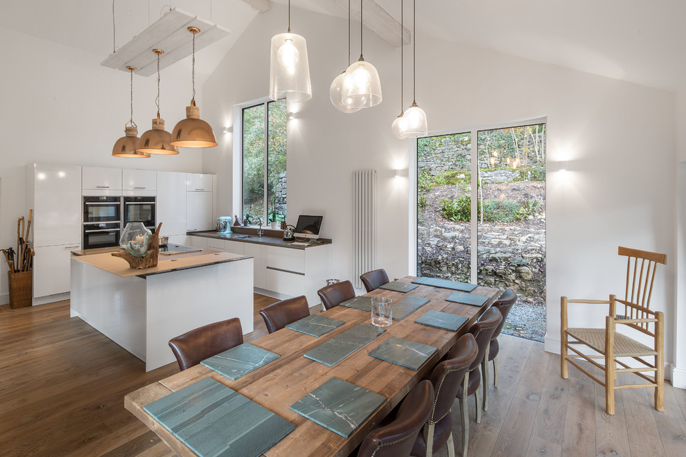 Réalisation d'une grande salle à manger ouverte sur la cuisine design avec un sol en bois brun, un sol marron, un mur blanc, une cheminée double-face et un manteau de cheminée en plâtre.