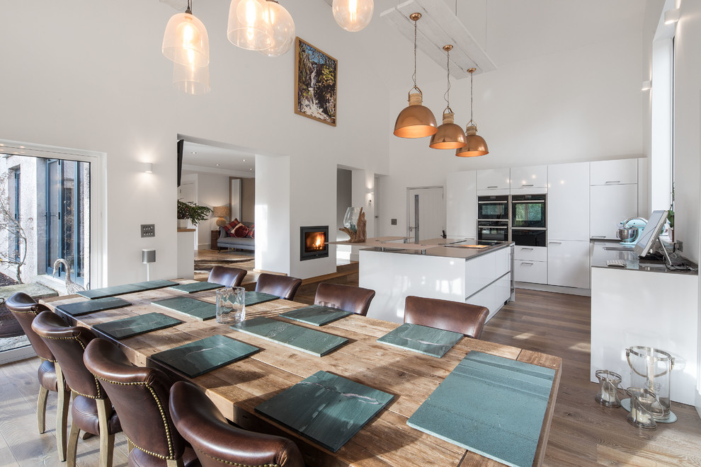 Exemple d'une grande salle à manger ouverte sur la cuisine tendance avec un sol en bois brun, un sol marron, un mur blanc, une cheminée double-face et un manteau de cheminée en plâtre.