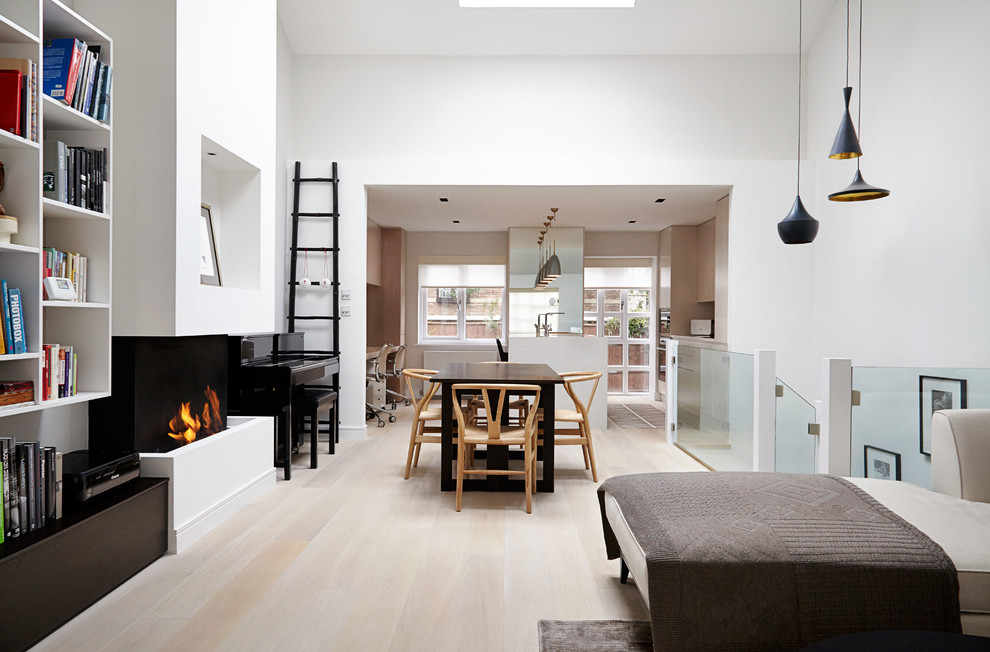 This is an example of a contemporary open plan dining room in London with a ribbon fireplace, a plastered fireplace surround, grey walls and light hardwood flooring.