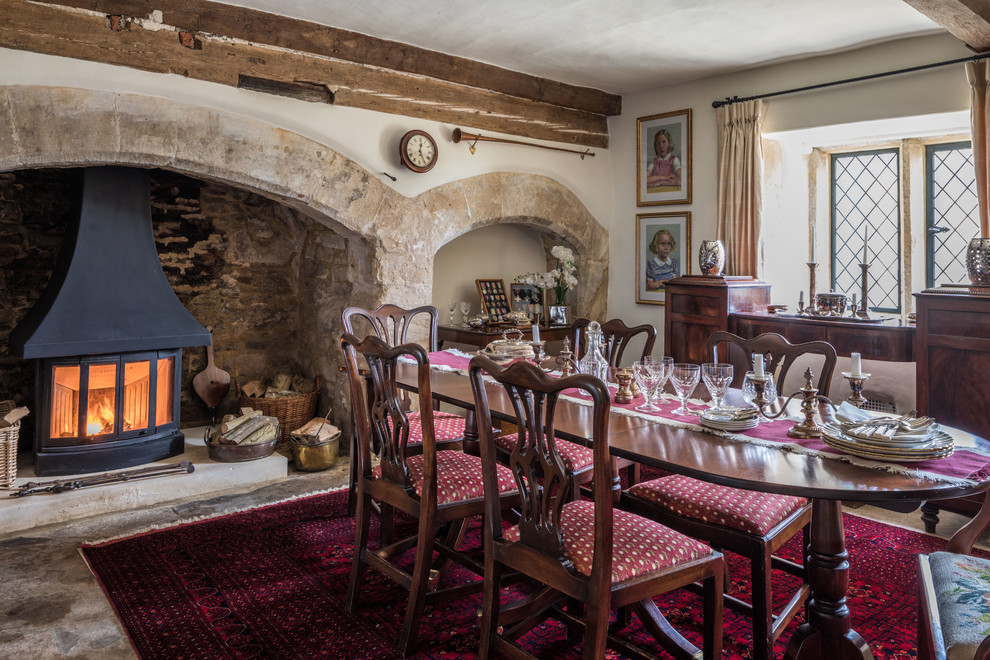 This is an example of a dining room in Wiltshire with limestone flooring, a wood burning stove and a stone fireplace surround.