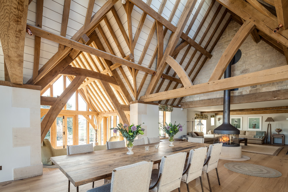 Immagine di una grande sala da pranzo aperta verso il soggiorno stile rurale con pareti bianche, parquet chiaro, stufa a legna e pavimento beige