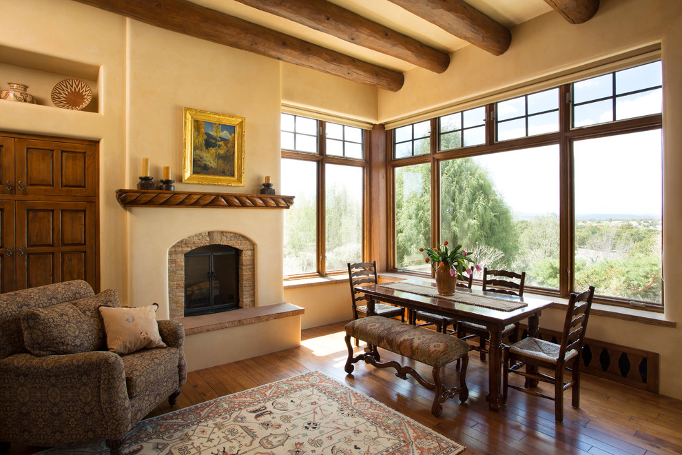 Inspiration pour une salle à manger ouverte sur le salon sud-ouest américain de taille moyenne avec un mur beige, un sol en bois brun, une cheminée standard et un manteau de cheminée en pierre.