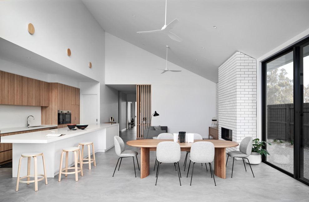 Exemple d'une grande salle à manger moderne avec un mur blanc, sol en béton ciré, un poêle à bois, un manteau de cheminée en brique et un sol gris.
