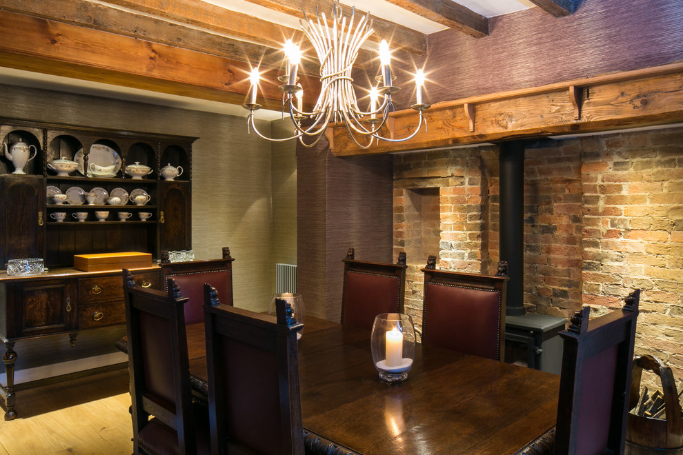 Idée de décoration pour une salle à manger tradition fermée et de taille moyenne avec parquet clair, un poêle à bois et un manteau de cheminée en brique.