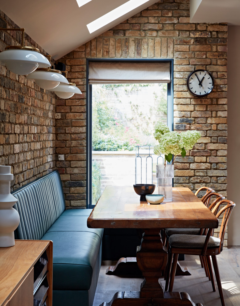 Cette photo montre une salle à manger ouverte sur la cuisine chic avec parquet clair, un mur en parement de brique, un mur blanc et aucune cheminée.