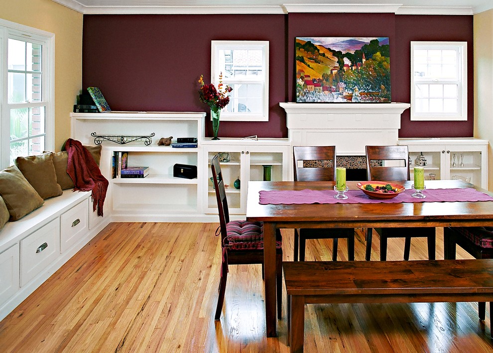 Immagine di una sala da pranzo aperta verso la cucina chic di medie dimensioni con pareti rosse, pavimento in legno massello medio, camino classico e cornice del camino in pietra