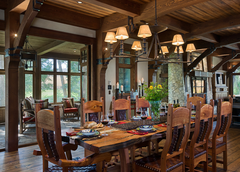 Cette photo montre une grande salle à manger ouverte sur le salon montagne avec un sol en bois brun, une cheminée standard et un manteau de cheminée en pierre.