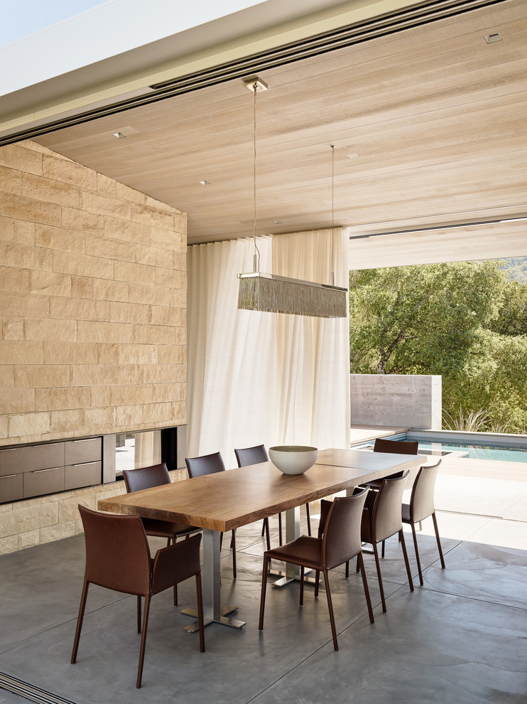 На фото: столовая в современном стиле с бетонным полом и двусторонним камином