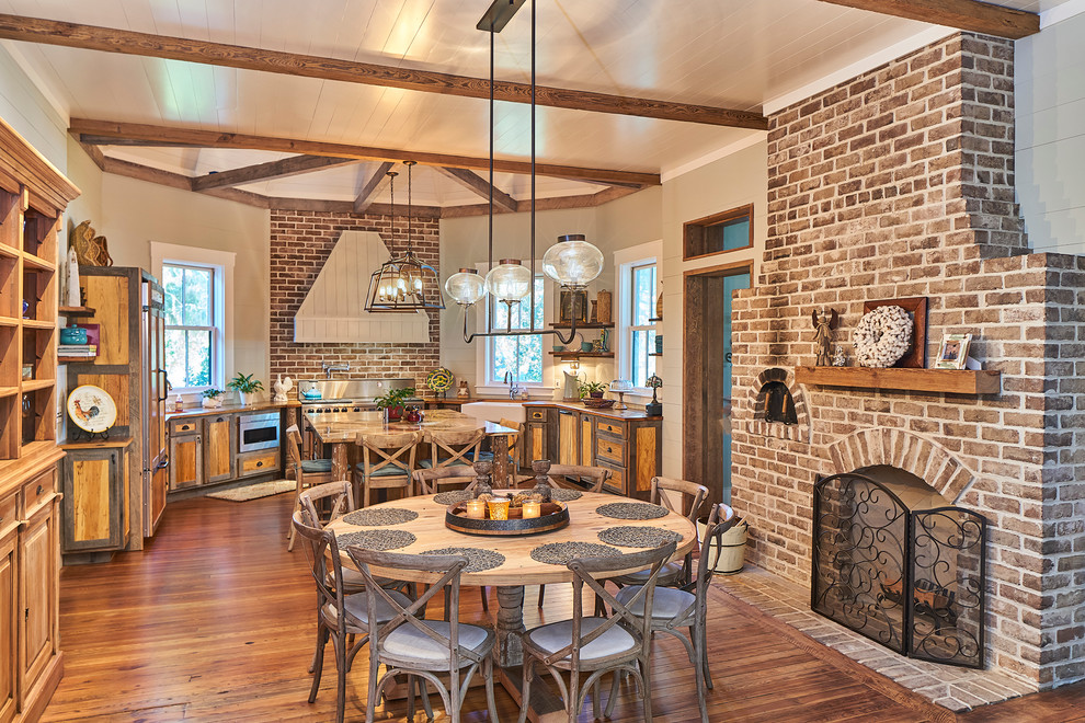 Aménagement d'une salle à manger ouverte sur la cuisine campagne avec un sol en bois brun, une cheminée standard et un manteau de cheminée en brique.