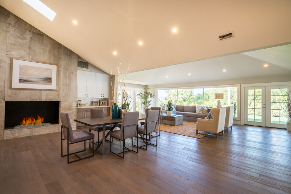 Cette image montre une très grande salle à manger ouverte sur la cuisine minimaliste avec un mur multicolore, un sol en bois brun, une cheminée standard, un manteau de cheminée en carrelage et un sol marron.