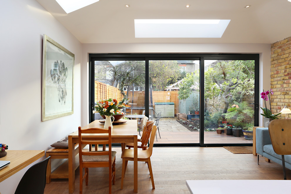 Contemporary open plan dining room in London with white walls, medium hardwood flooring and brown floors.