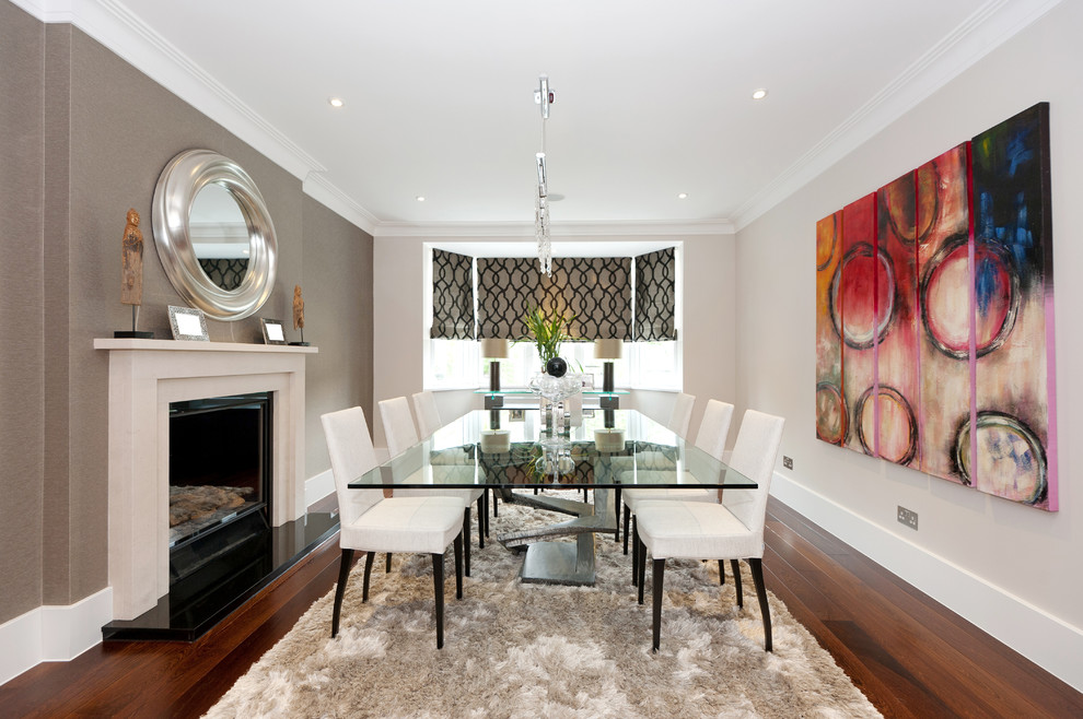 Photo of a medium sized contemporary dining room in London with beige walls, dark hardwood flooring, a standard fireplace and feature lighting.