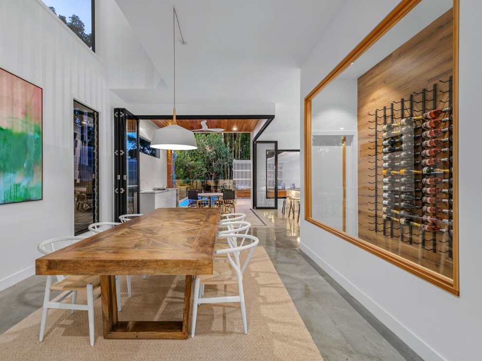 Cette image montre une grande salle à manger ouverte sur le salon minimaliste avec un mur blanc, sol en béton ciré et un sol gris.