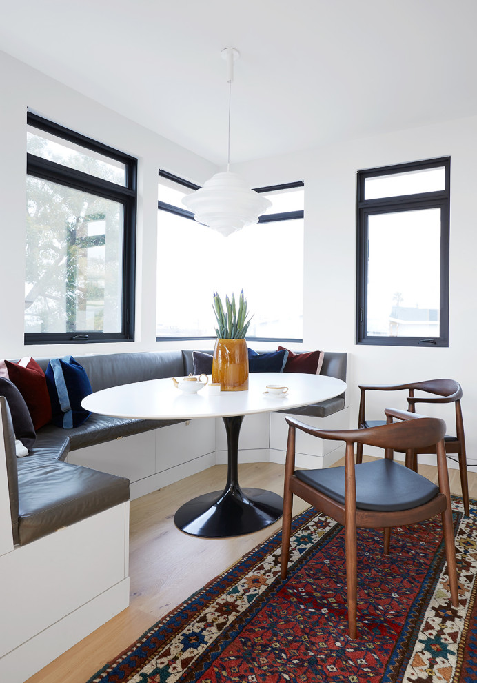 Cette image montre une salle à manger design avec parquet clair, une banquette d'angle, un mur blanc et un sol beige.