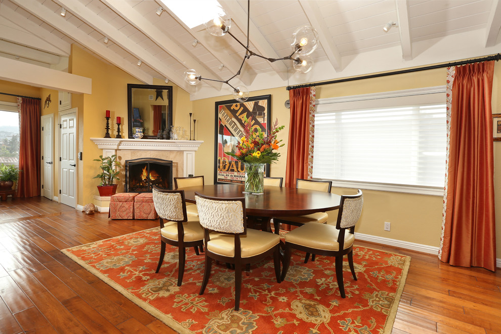 Cette photo montre une salle à manger ouverte sur le salon chic de taille moyenne avec un mur jaune, un sol en bois brun, une cheminée d'angle, un manteau de cheminée en plâtre et un sol marron.