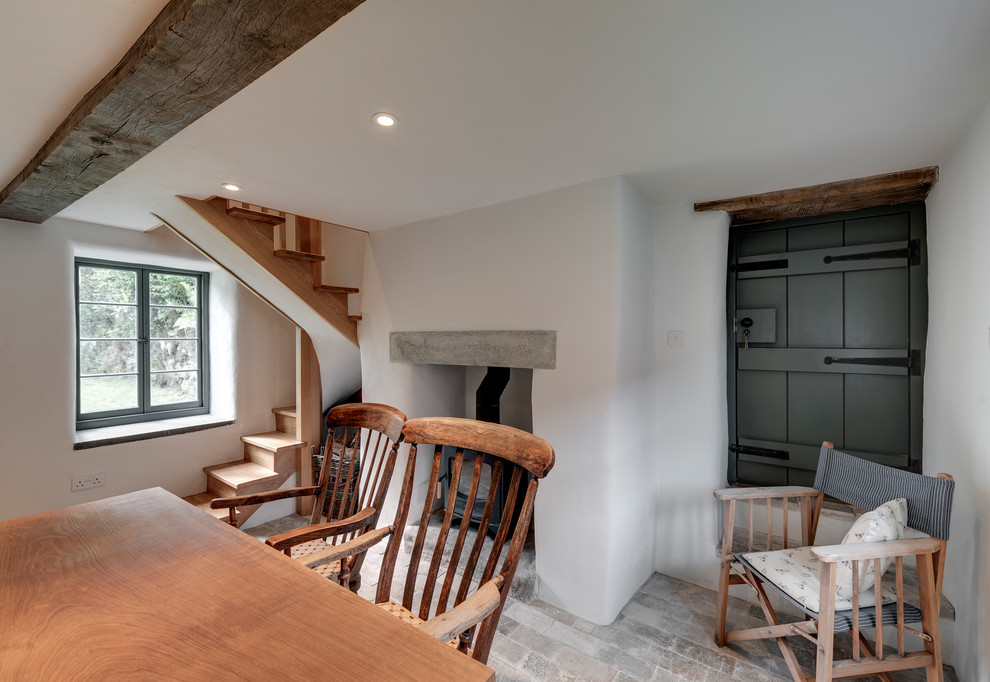 Idées déco pour une petite salle à manger classique fermée avec un mur blanc, un sol en brique, un poêle à bois, un manteau de cheminée en plâtre et un sol beige.
