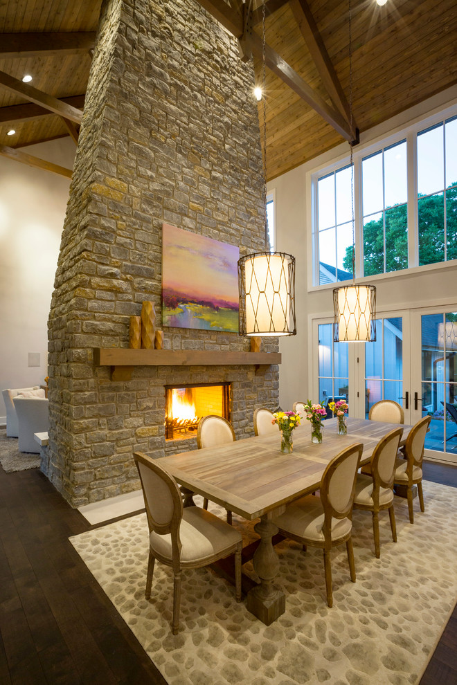 Aménagement d'une salle à manger ouverte sur la cuisine campagne avec un mur gris, parquet foncé, une cheminée double-face et un manteau de cheminée en pierre.