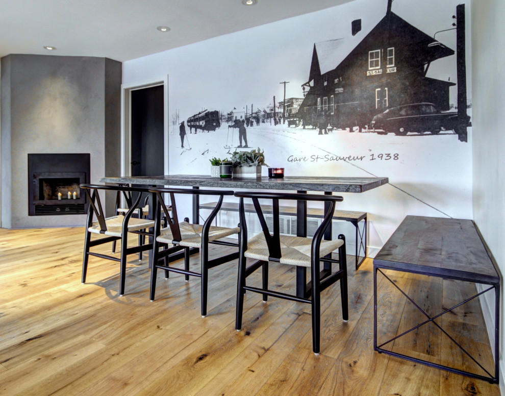 Photo of a large rustic dining room in Montreal with banquette seating, white walls, medium hardwood flooring, a corner fireplace, a concrete fireplace surround and wallpapered walls.