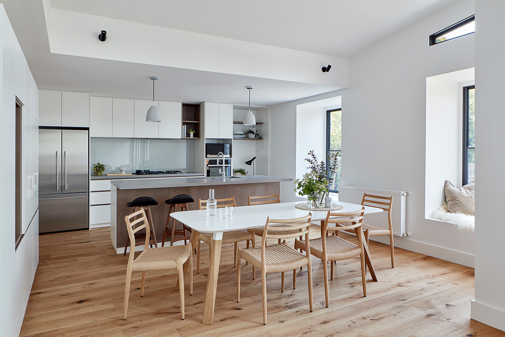 Réalisation d'une salle à manger ouverte sur la cuisine design de taille moyenne avec un mur blanc, parquet clair, un sol marron et un plafond voûté.
