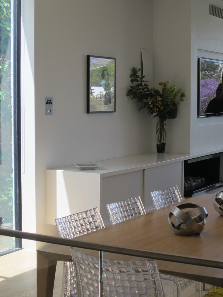 Exemple d'une salle à manger tendance de taille moyenne avec un mur blanc, parquet clair et un manteau de cheminée en pierre.