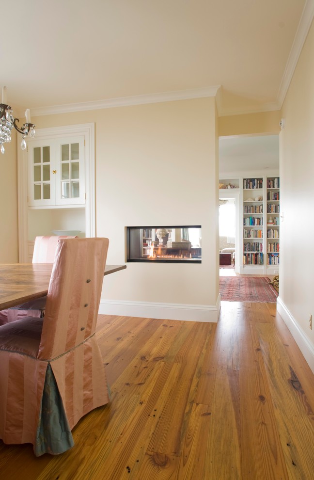 Inspiration for a large timeless medium tone wood floor enclosed dining room remodel in Portland Maine with yellow walls, a two-sided fireplace and a plaster fireplace