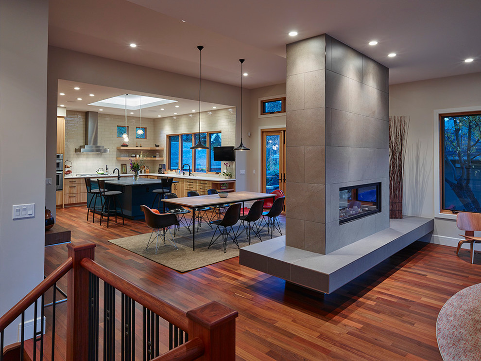 Moderne Wohnküche mit beiger Wandfarbe, braunem Holzboden, Tunnelkamin und gefliester Kaminumrandung in Calgary
