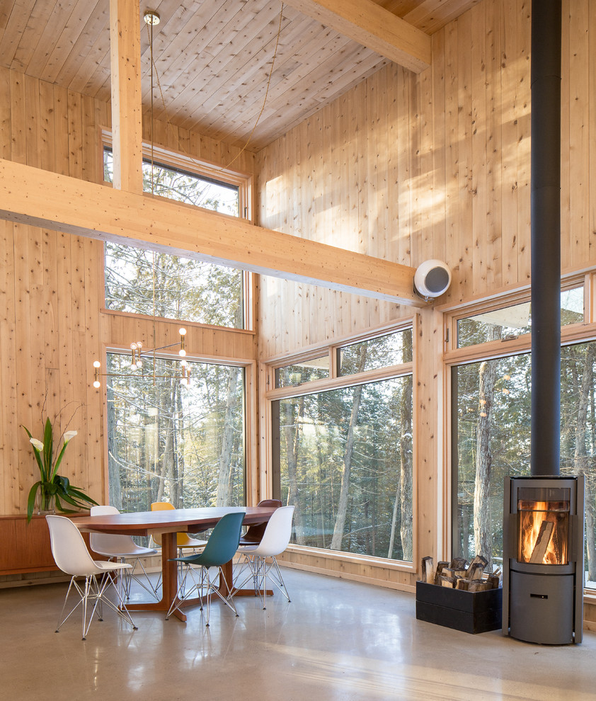 Immagine di una sala da pranzo aperta verso il soggiorno stile rurale di medie dimensioni con pavimento in cemento e stufa a legna