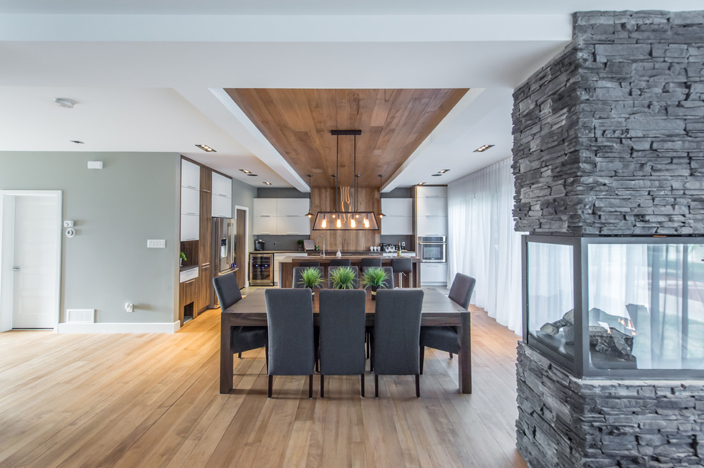 Exemple d'une salle à manger ouverte sur le salon tendance avec une cheminée double-face, un mur gris et un sol en bois brun.