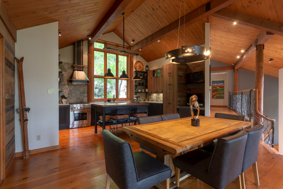 Exemple d'une salle à manger ouverte sur la cuisine montagne de taille moyenne avec un mur blanc, un sol en bois brun, un manteau de cheminée en pierre et un sol orange.