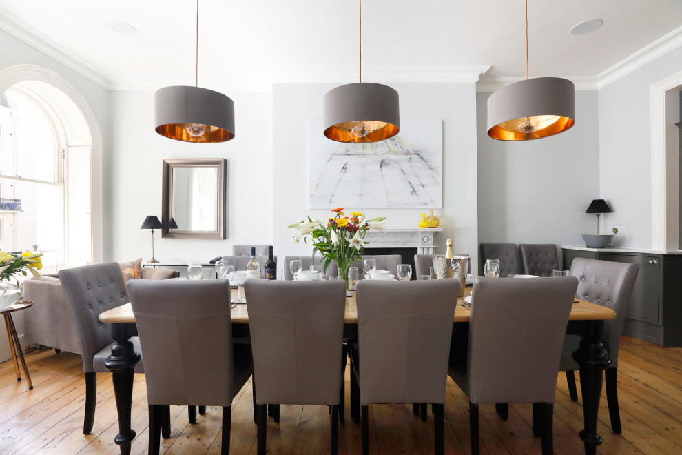 Стильный дизайн: большая кухня-столовая в стиле неоклассика (современная классика) с серыми стенами, паркетным полом среднего тона, стандартным камином, фасадом камина из камня и коричневым полом - последний тренд