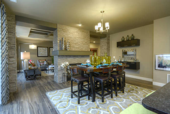 Cette photo montre une salle à manger ouverte sur la cuisine tendance avec un mur gris, un sol en bois brun, une cheminée double-face et un manteau de cheminée en pierre.