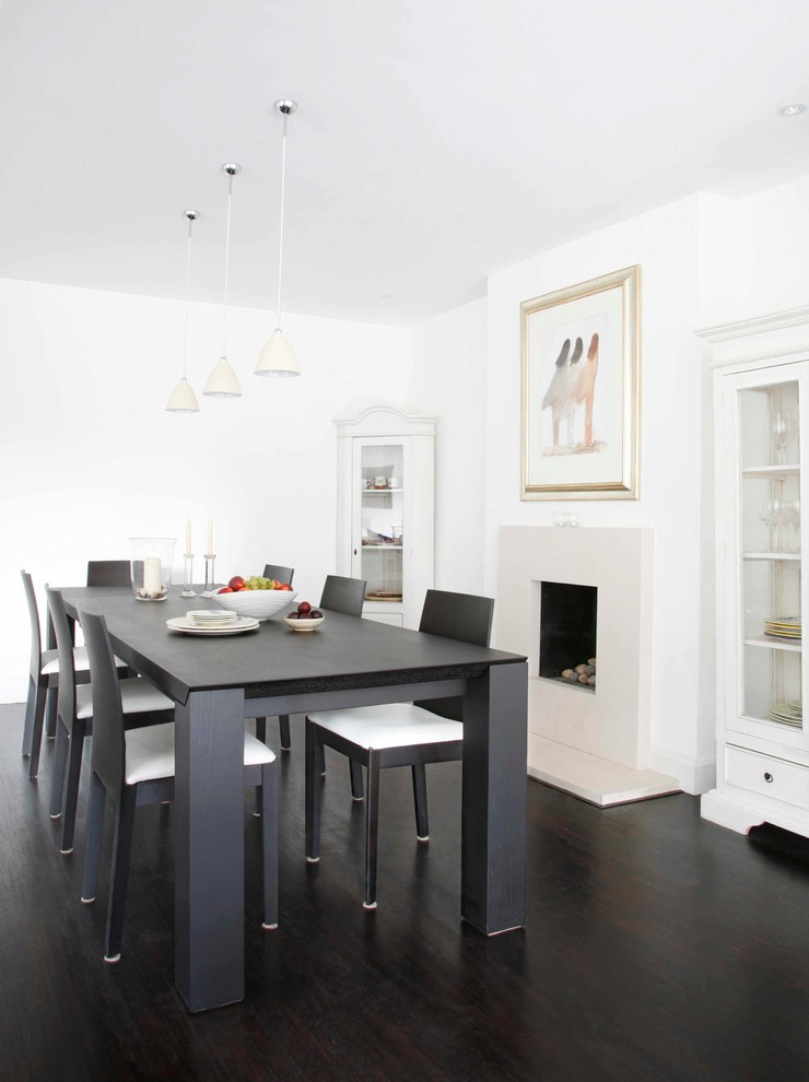 Cette image montre une salle à manger ouverte sur la cuisine traditionnelle de taille moyenne avec un mur blanc, un manteau de cheminée en pierre, parquet foncé et un sol marron.