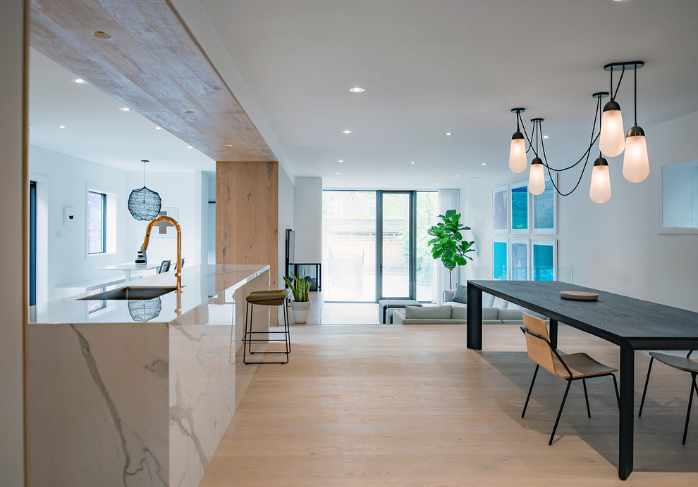 Foto di una sala da pranzo aperta verso la cucina minimalista di medie dimensioni con pareti bianche, parquet chiaro, nessun camino e pavimento marrone
