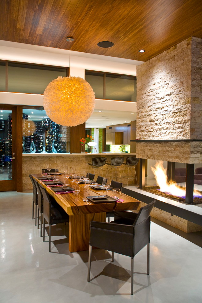 Exemple d'une salle à manger tendance avec sol en béton ciré, une cheminée double-face et un manteau de cheminée en pierre.