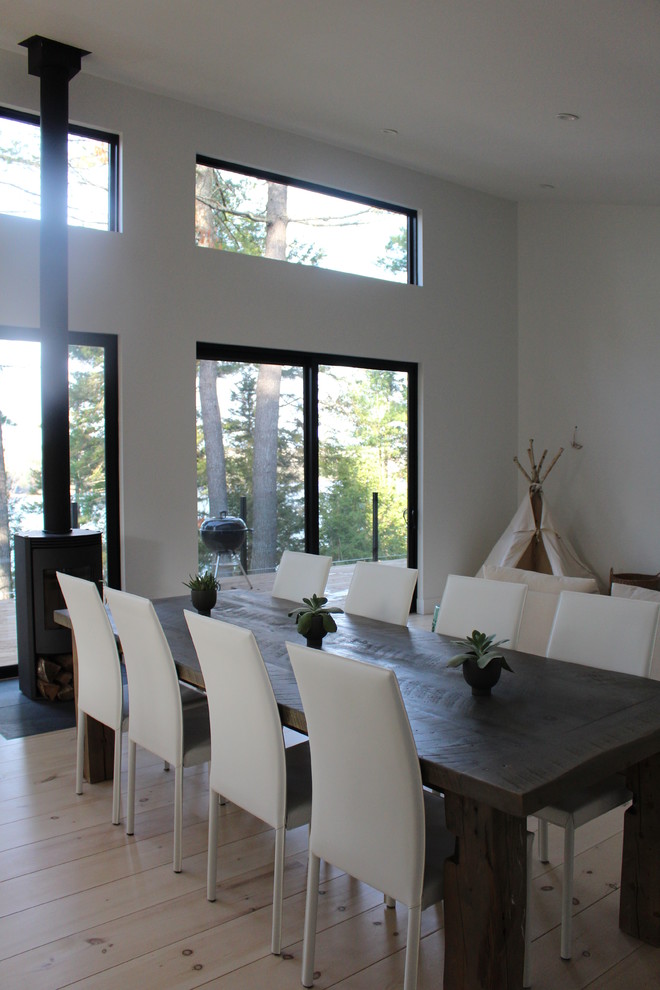 Idées déco pour une salle à manger ouverte sur le salon moderne avec un mur blanc, un sol en contreplaqué, un poêle à bois et un manteau de cheminée en pierre.