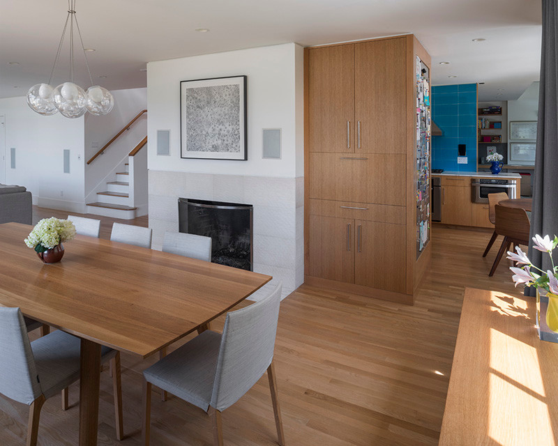 Aménagement d'une salle à manger ouverte sur le salon moderne avec un mur blanc, parquet clair, une cheminée standard et un manteau de cheminée en carrelage.