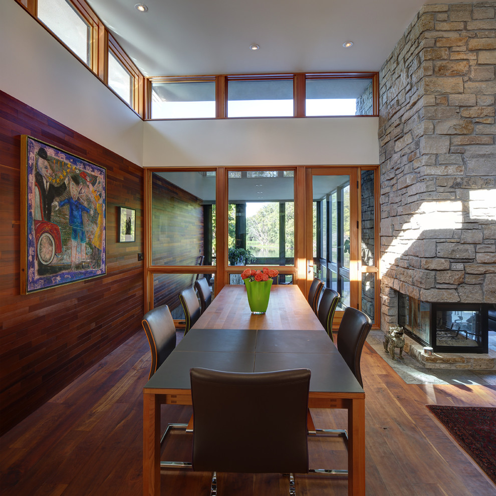 Inspiration for a modern medium tone wood floor dining room remodel in Milwaukee with a two-sided fireplace and a stone fireplace