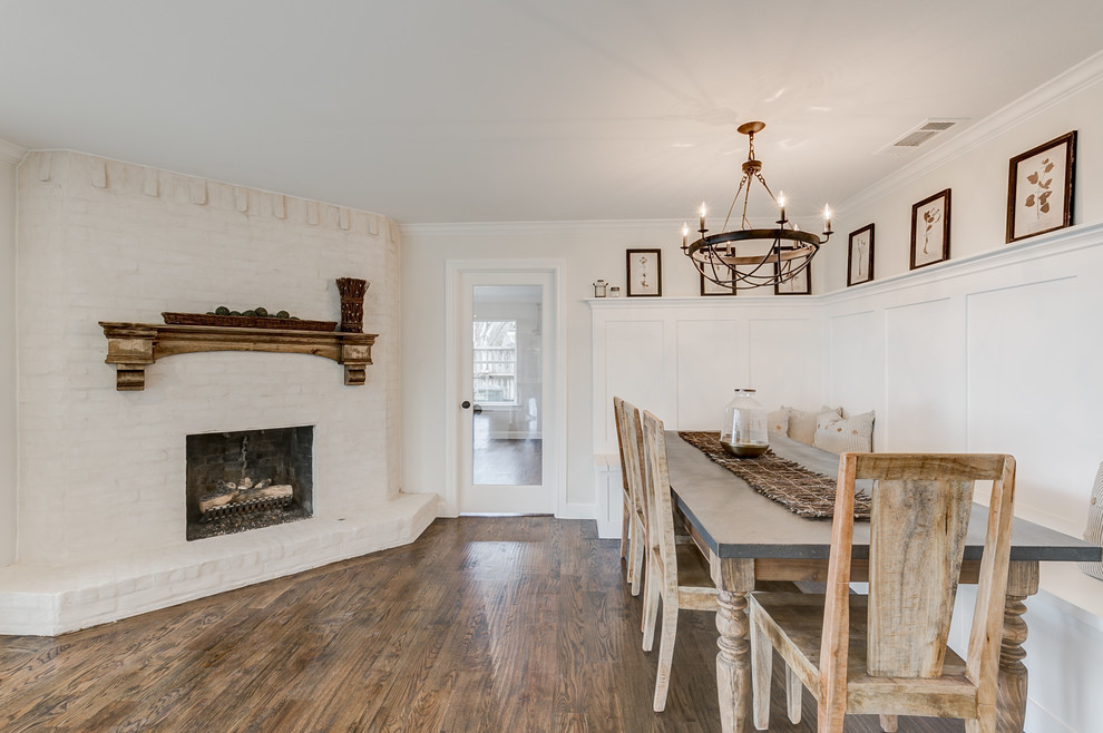Cette photo montre une grande salle à manger ouverte sur la cuisine nature avec un mur blanc, un sol en bois brun, une cheminée d'angle, un manteau de cheminée en brique et un sol marron.
