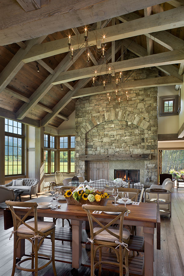 Inspiration pour une salle à manger ouverte sur la cuisine chalet avec un sol en bois brun, une cheminée standard et un manteau de cheminée en pierre.