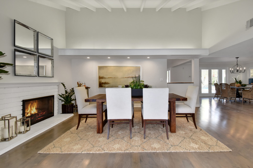 Idée de décoration pour une salle à manger ouverte sur le salon tradition avec un mur blanc, un sol en bois brun, une cheminée standard, un manteau de cheminée en brique et un sol gris.