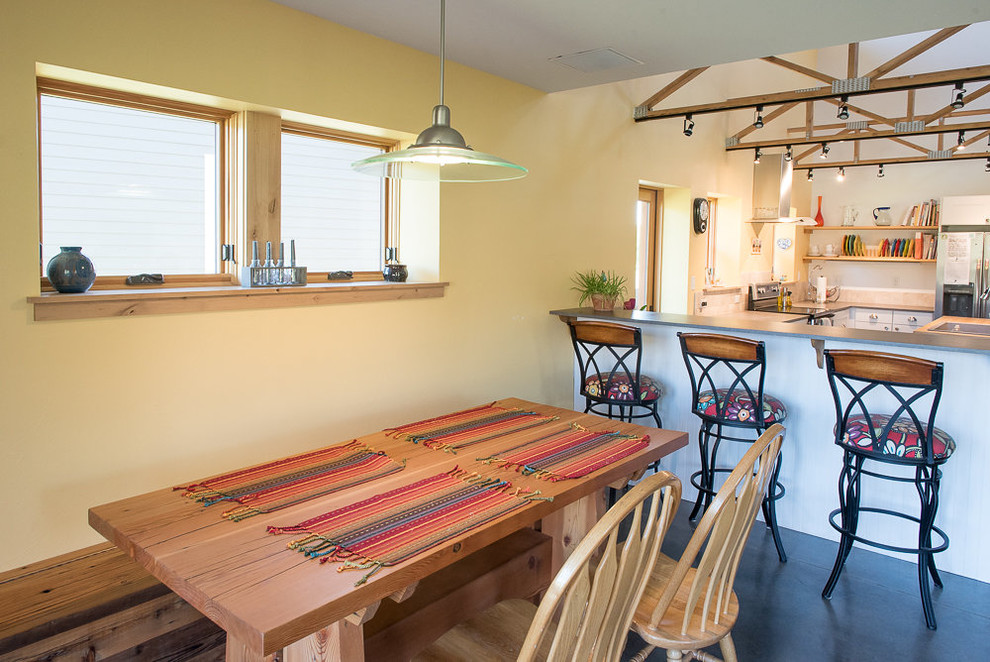 Cette image montre une petite salle à manger ouverte sur la cuisine chalet avec un mur jaune, sol en béton ciré, aucune cheminée et un sol gris.