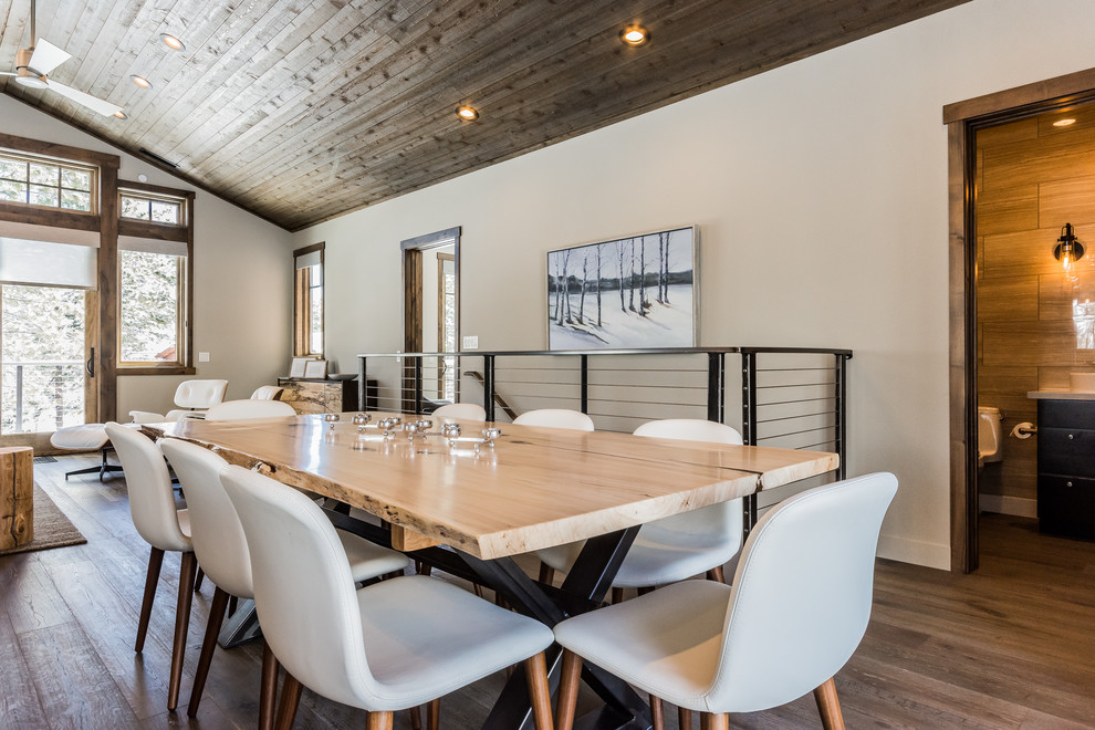 Réalisation d'une salle à manger ouverte sur la cuisine chalet de taille moyenne avec un mur gris, un sol en bois brun, une cheminée d'angle, un manteau de cheminée en pierre et un sol gris.