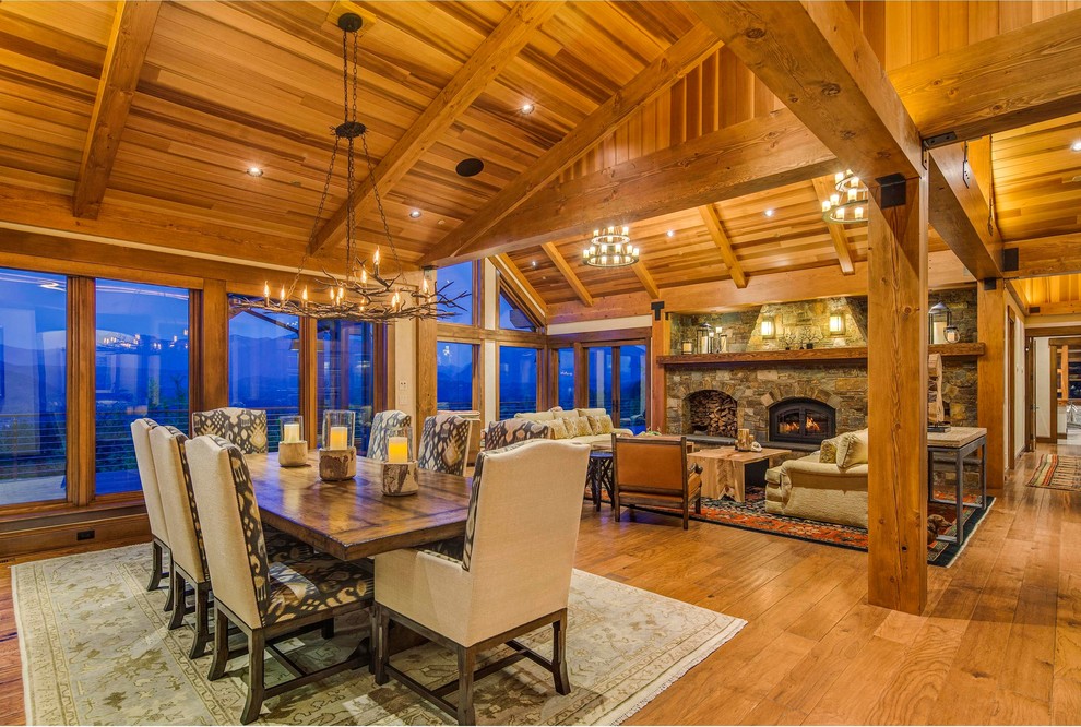 Cette image montre une grande salle à manger ouverte sur le salon chalet avec une cheminée standard et un manteau de cheminée en pierre.