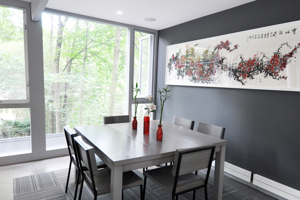 Inspiration pour une salle à manger ouverte sur le salon minimaliste de taille moyenne avec un mur gris, un sol en bois brun, une cheminée double-face et un manteau de cheminée en brique.