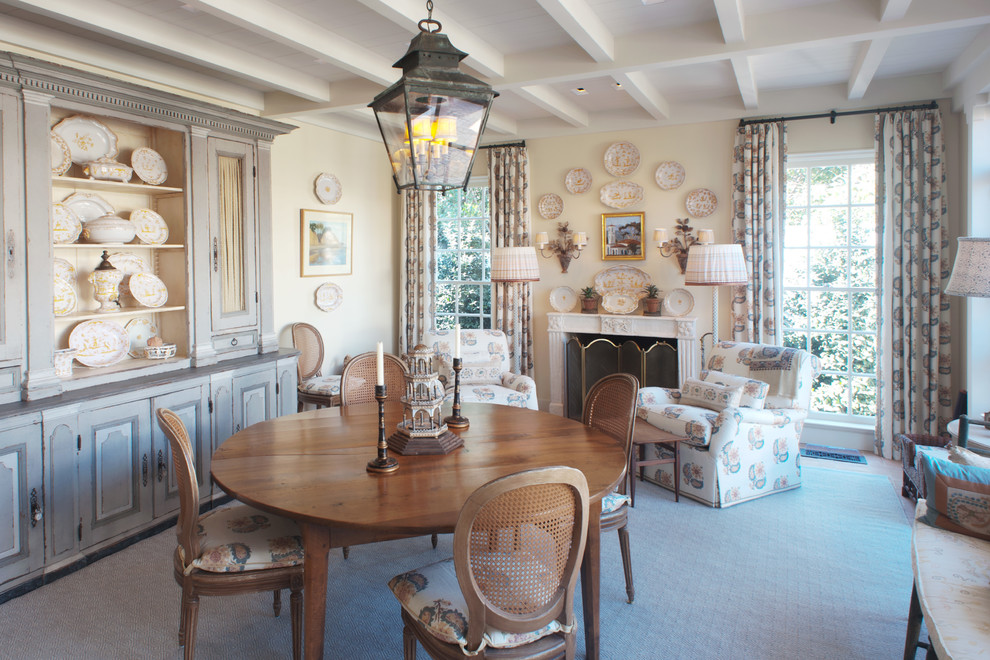Cette image montre une salle à manger ouverte sur le salon traditionnelle de taille moyenne avec un mur beige, une cheminée standard, un manteau de cheminée en plâtre, un sol beige et tomettes au sol.