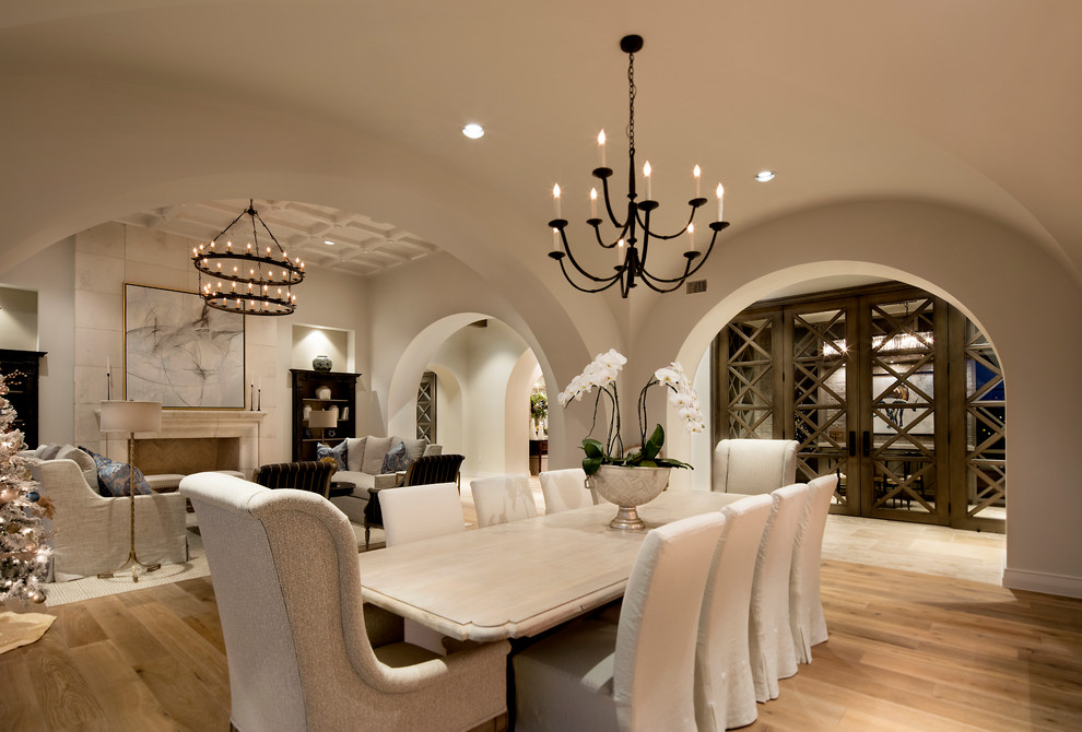 Cette image montre une grande salle à manger ouverte sur le salon méditerranéenne avec un sol en bois brun, un manteau de cheminée en pierre, un mur beige, une cheminée standard et un sol marron.