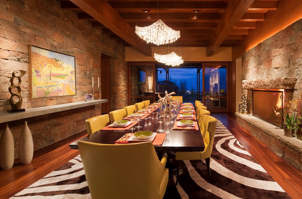 Cette image montre une très grande salle à manger sud-ouest américain fermée avec un sol en bois brun, une cheminée standard, un mur multicolore, un sol marron et un manteau de cheminée en pierre.