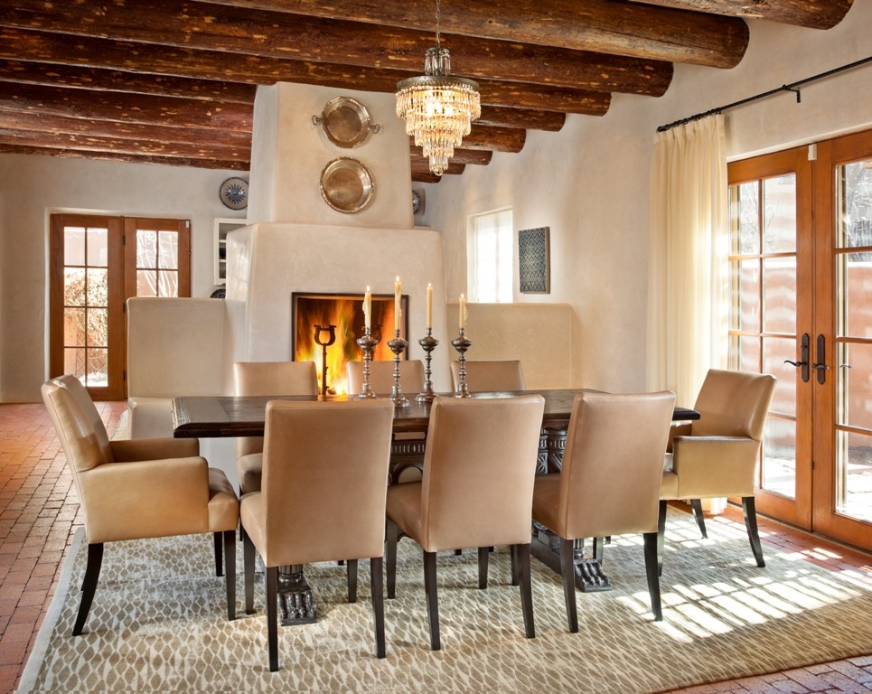 Cette photo montre une salle à manger sud-ouest américain avec un mur beige, un sol en brique, un manteau de cheminée en plâtre et une cheminée standard.