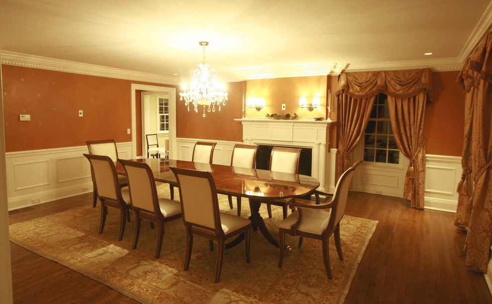 Cette photo montre une salle à manger chic fermée et de taille moyenne avec un mur orange, un sol en bois brun et une cheminée standard.