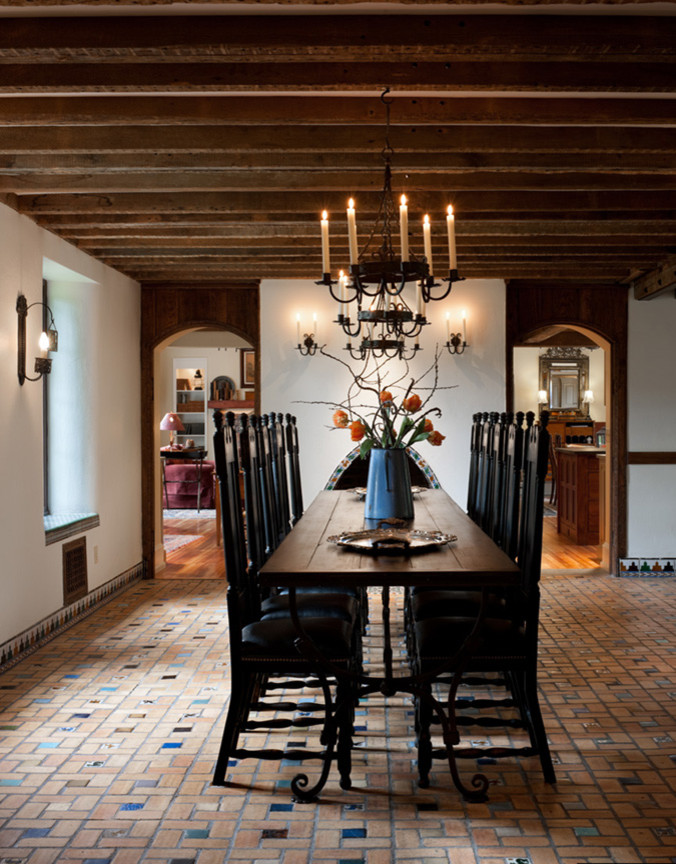 Immagine di una grande sala da pranzo aperta verso la cucina classica con pareti bianche, camino classico, cornice del camino piastrellata e pavimento in mattoni
